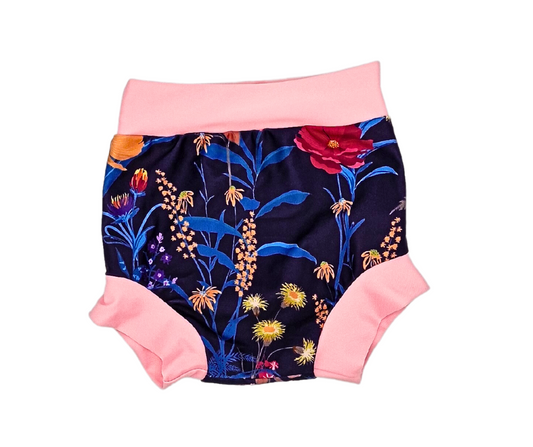 Die Lumina Schwimmwindel Pull Up ist ein Paar Baby-Shorts mit buntem Blumendruck auf dunklem Stoff und hellrosa Bund und Beinbündchen, die für einen bequemen Sitz beim Wasserspaß sorgen.