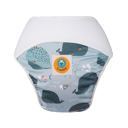 Der Lumina Pull-me-Up All in One Windel One-Size hat ein hellblaues Wal- und Fischmotiv, einen weißen Bund, einen gelben Lumina-Logoaufnäher, eine hohe Saugfähigkeit und ist aus GOTS-zertifizierter Bio-Baumwolle hergestellt.