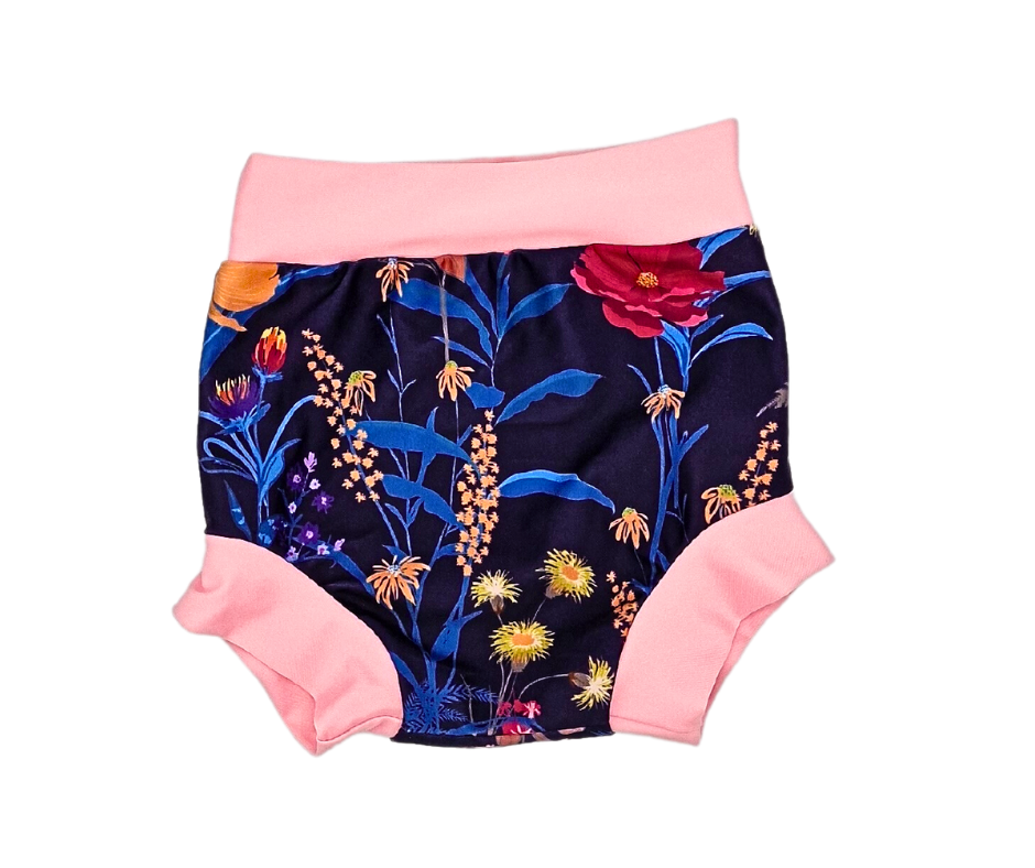 Die Lumina Schwimmwindel Pull Up ist ein Paar Baby-Shorts mit buntem Blumendruck auf dunklem Stoff und hellrosa Bund und Beinbündchen, die für einen bequemen Sitz beim Wasserspaß sorgen.