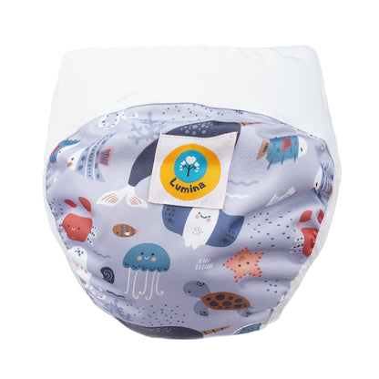 Der Lumina Pull-me-Up All in One Windel One-Size zeichnet sich durch ein lebhaftes Meerestiermotiv mit Walen, Quallen, Schildkröten und Fischen, ein weißes Abschlussband, hohes Saugvolumen und einen gelben Lumina-Anhänger auf der Vorderseite aus.