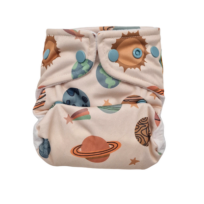 Die Lumina Überhose für Neugeborene ist eine wiederverwendbare Stoffwindel mit blauen Druckknöpfen, die bunte Planeten, Sterne und Sonnen auf einem hellbeigen Minky Fleece Hintergrund zeigt.
