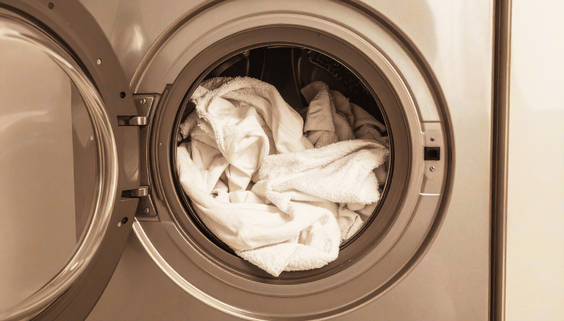 Eine Frontlader-Waschmaschine mit geöffneter Tür, in der ein Stapel weißer Handtücher und Wäsche zum Waschen bereit liegt.